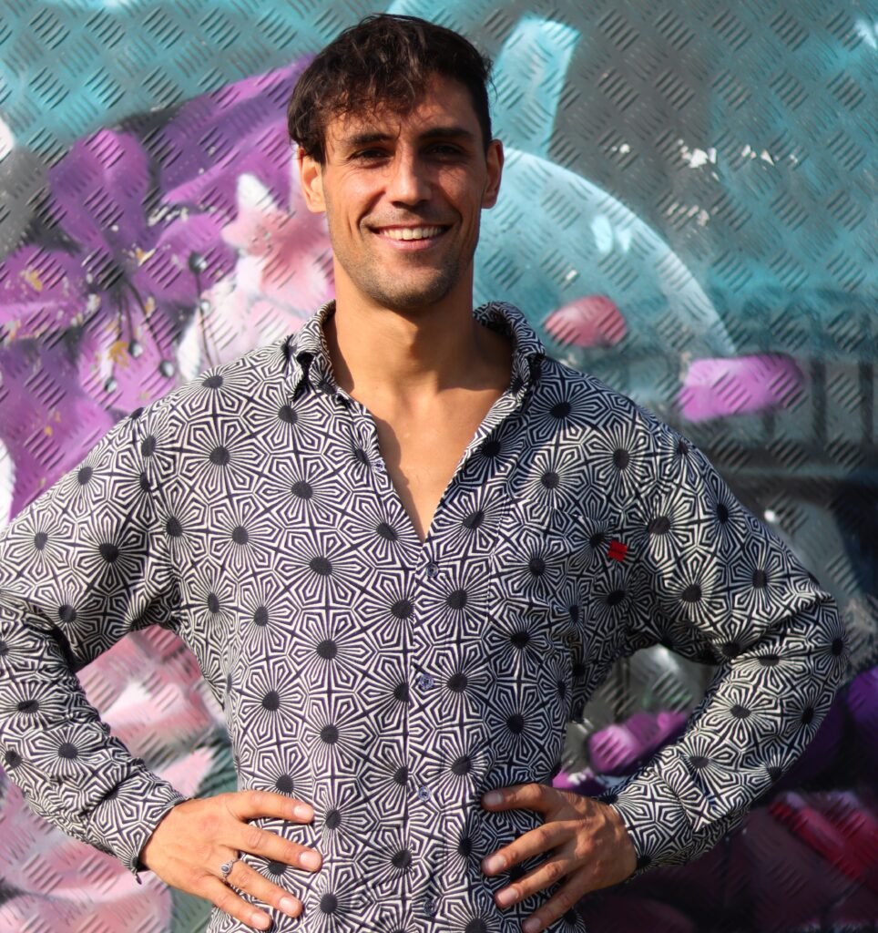 Benjamin Malik – Coach für persönliche Entwicklung, Selbstvertrauen und Transformation – mit offenem Lächeln vor kreativem Hintergrund.