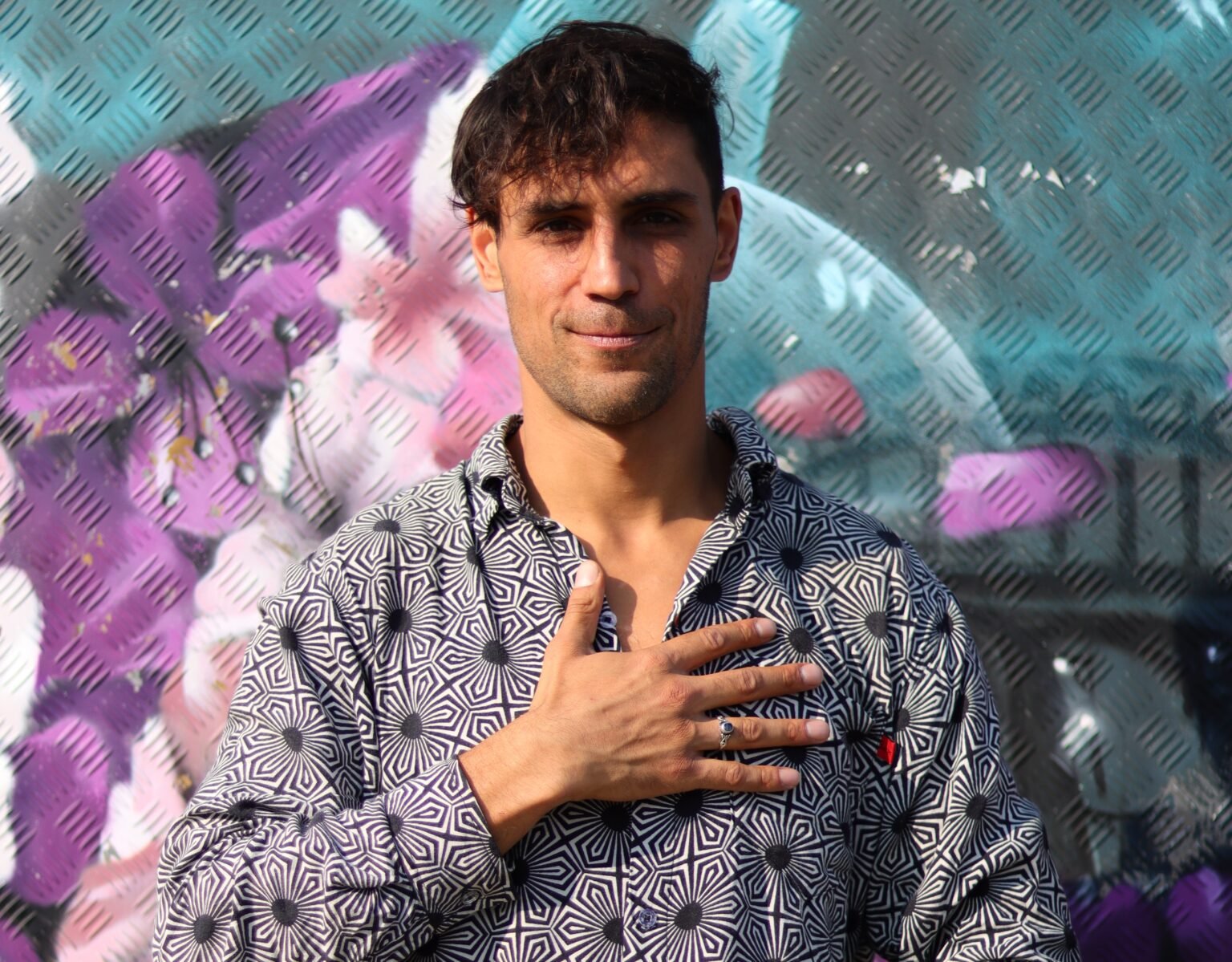 Benjamin Malik mit Hand auf dem Herz, vor bunter Wand – Verkörperte Herzkraft Workshop für Selbstbewusstsein, Verbindung & Heilung.