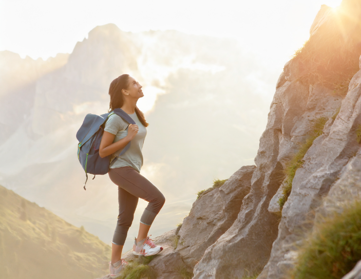 Eine Frau mit Rucksack erklimmt einen Berg – Symbol für persönliches Wachstum, innere Stärke und neue Perspektiven durch Coaching.