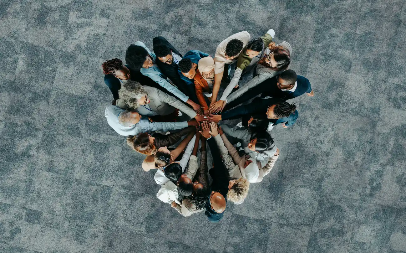 Eine Gruppe Menschen legt ihre Hände zusammen und formt ein Herz – Symbol für Bewusstsein, Präsenz, Verbindung und gemeinsame Lebendigkeit