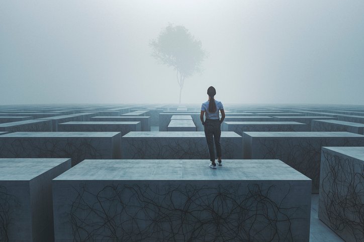 Frau steht auf einer Mauer, blickt auf ein Labyrinth und einen Baum – symbolisiert Herzöffnung, Schutz und innere Stärke