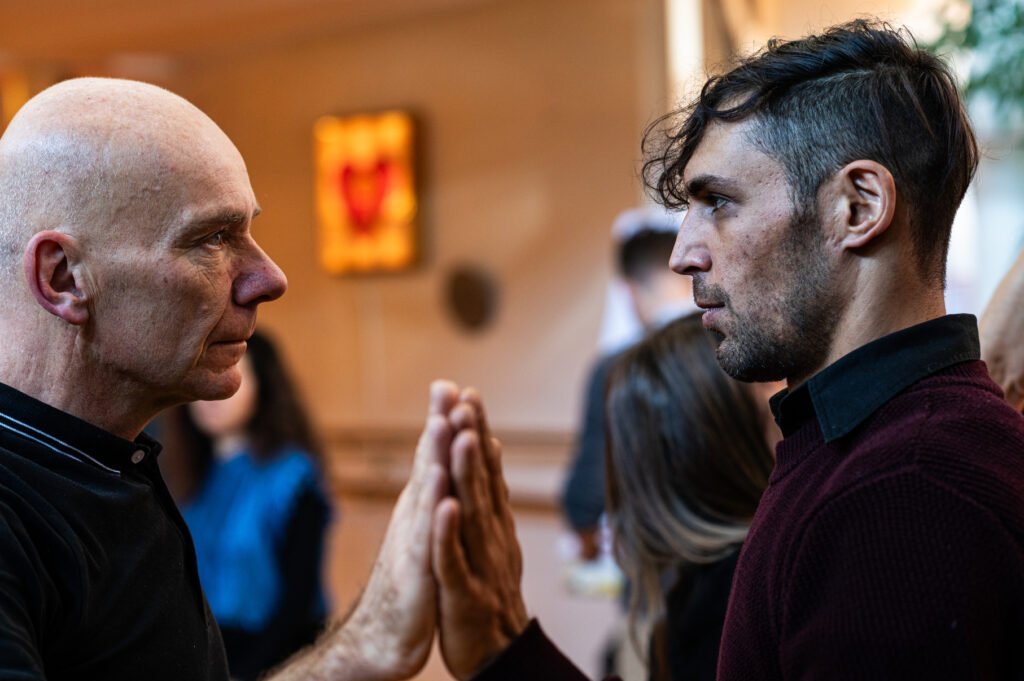 Zwei Männer stehen sich gegenüber, Hände berühren sich – bewusster Kontakt, Abgrenzung und verkörperte Präsenz im Raum